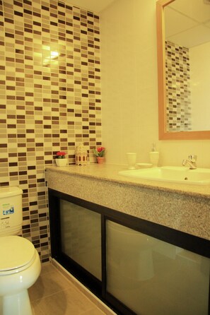 A bathroom with a tiled backsplash, a sink, a mirror, and a toilet. - iPREMIUM Sukhumvit 81 (Bangkok)