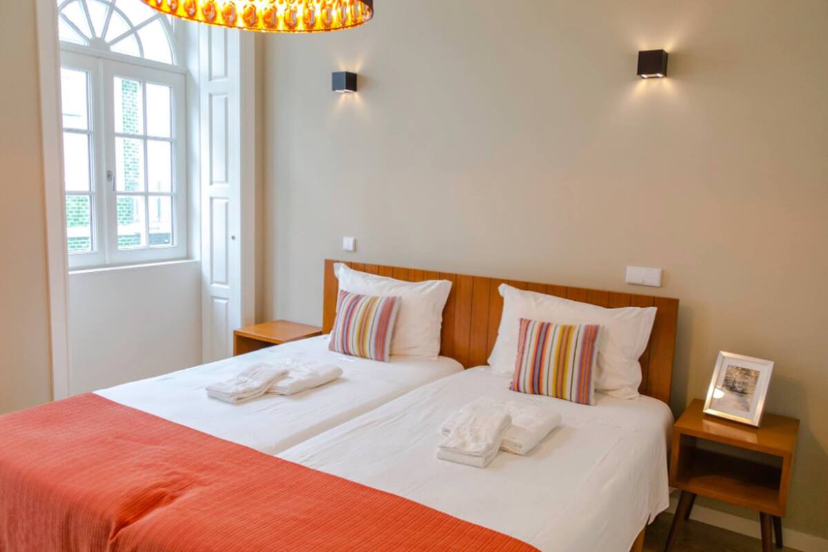 Une chambre d’hôtel avec deux lits, une grande fenêtre et un lustre.