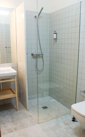 Een douche met glazen deur, een wastafel en een toilet in een betegelde badkamer.