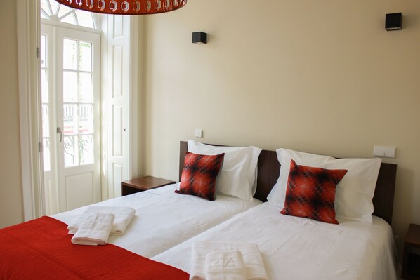 Een hotelkamer met twee bedden, witte lakens, kussens met een rood en zwart patroon, en een rode plaid.