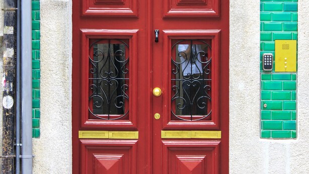 Eine rote Doppeltür mit einer Nummernschild, ein Fenster mit schmiedeeisernen Gittern und eine grüne Kachelwand.
