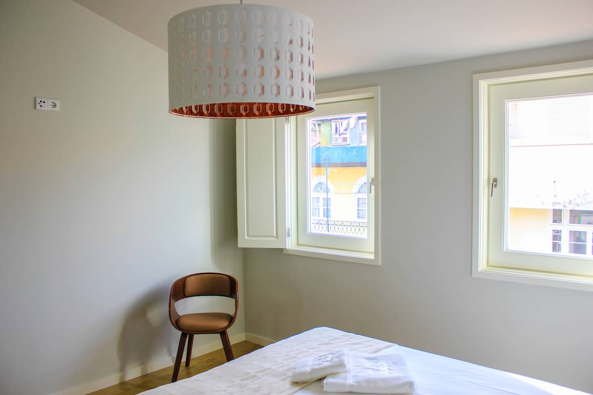 Une chambre à coucher avec un lit, une chaise, une fenêtre et un luminaire suspendu.