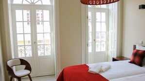Ein Hotelzimmer mit einem Bett, zwei weißen Handtüchern, einer roten Tagesdecke, einem Holzstuhl und einer Tür mit Blick auf einen Balkon.