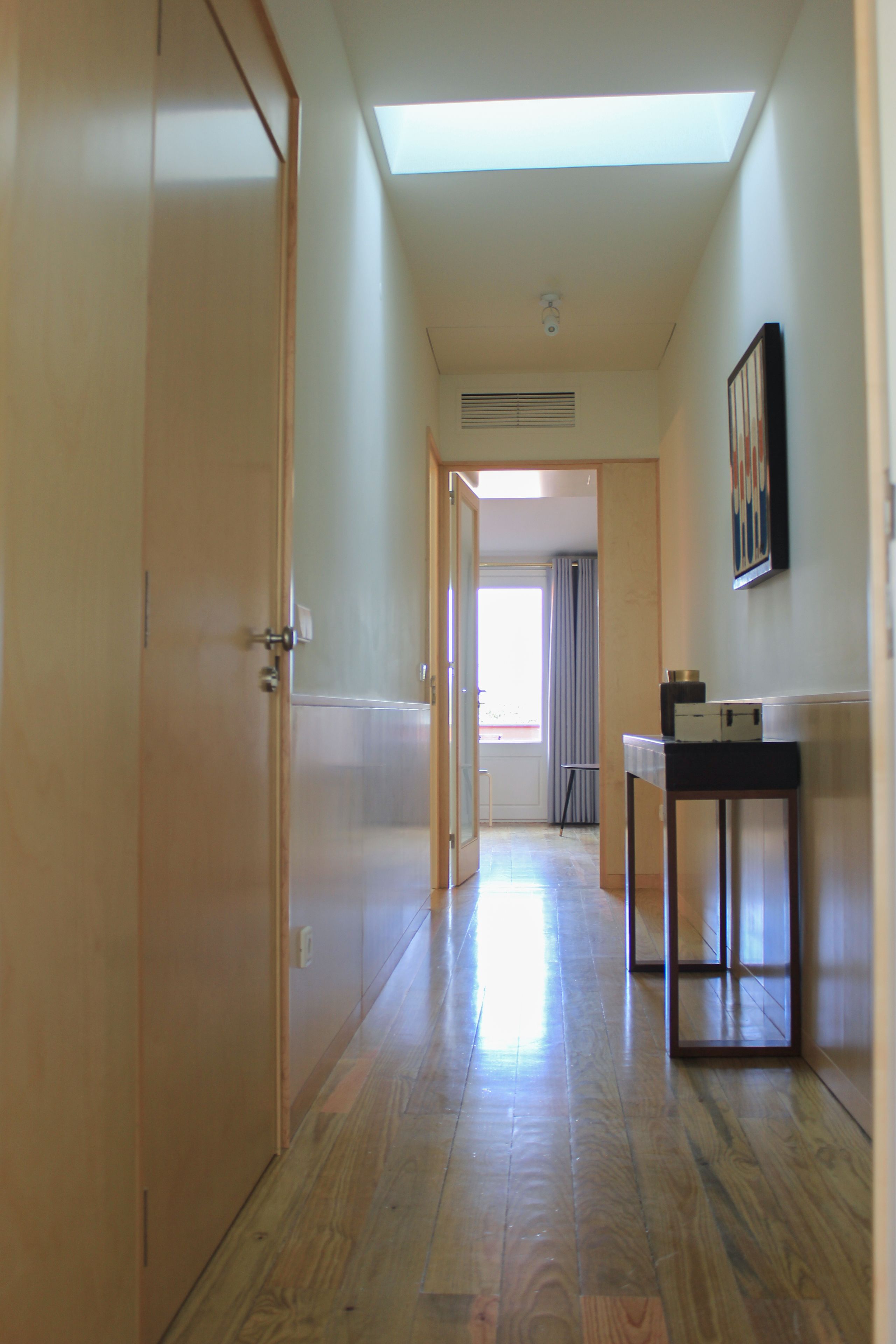 A hallway with wooden doors, a skylight, and a small table with items on it.