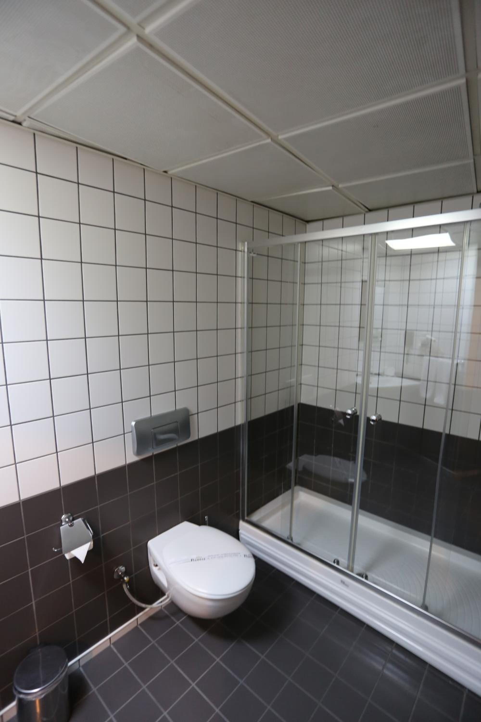 Een badkamer met toilet, prullenbak en een douchecabine met glazen wanden.