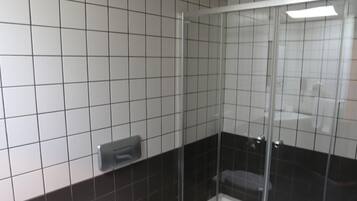 Een badkamer met toilet, prullenbak en een douchecabine met glazen wanden.
