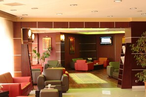 Un vestíbulo de hotel con varias zonas de estar, una pantalla de televisión y un mostrador de recepción.