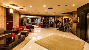 Un hall d’entrée spacieux au design moderne, comprenant un coin salon avec des canapés rouges, une table basse et un escalier menant à un niveau supérieur.