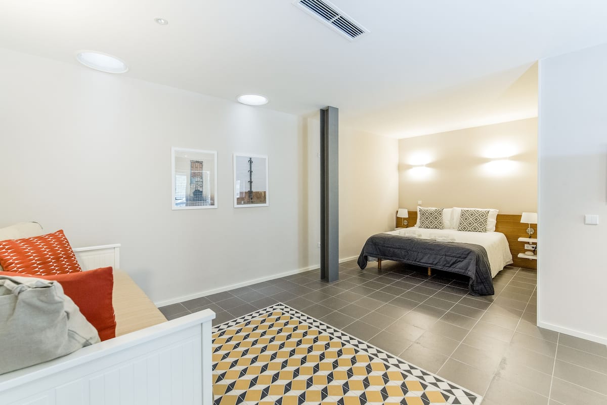 A modern bedroom with a bed, a nightstand, a chair, and a patterned rug.