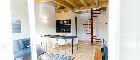 A modern kitchen with a dining area, wooden ceiling beams, and a staircase with red railings.