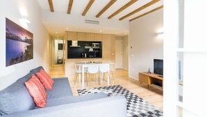 A modern living room with a grey sofa, red pillows, a checkered rug, a dining area with a white table and chairs, and a kitchen with wooden cabinets and a TV. - Oporto Trendy River (Porto)