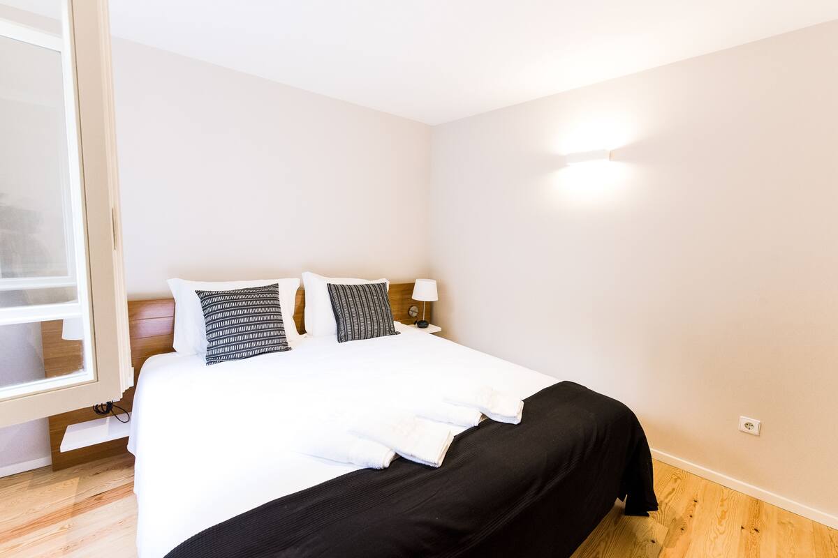 A neatly made bed with white and black bedding, a wooden headboard, and a bedside table with a lamp.
