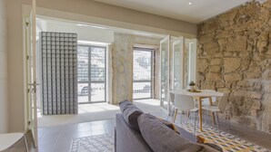 A modern living room with a sofa, a dining table with chairs, and a stone wall. - Oporto Trendy River (Porto)