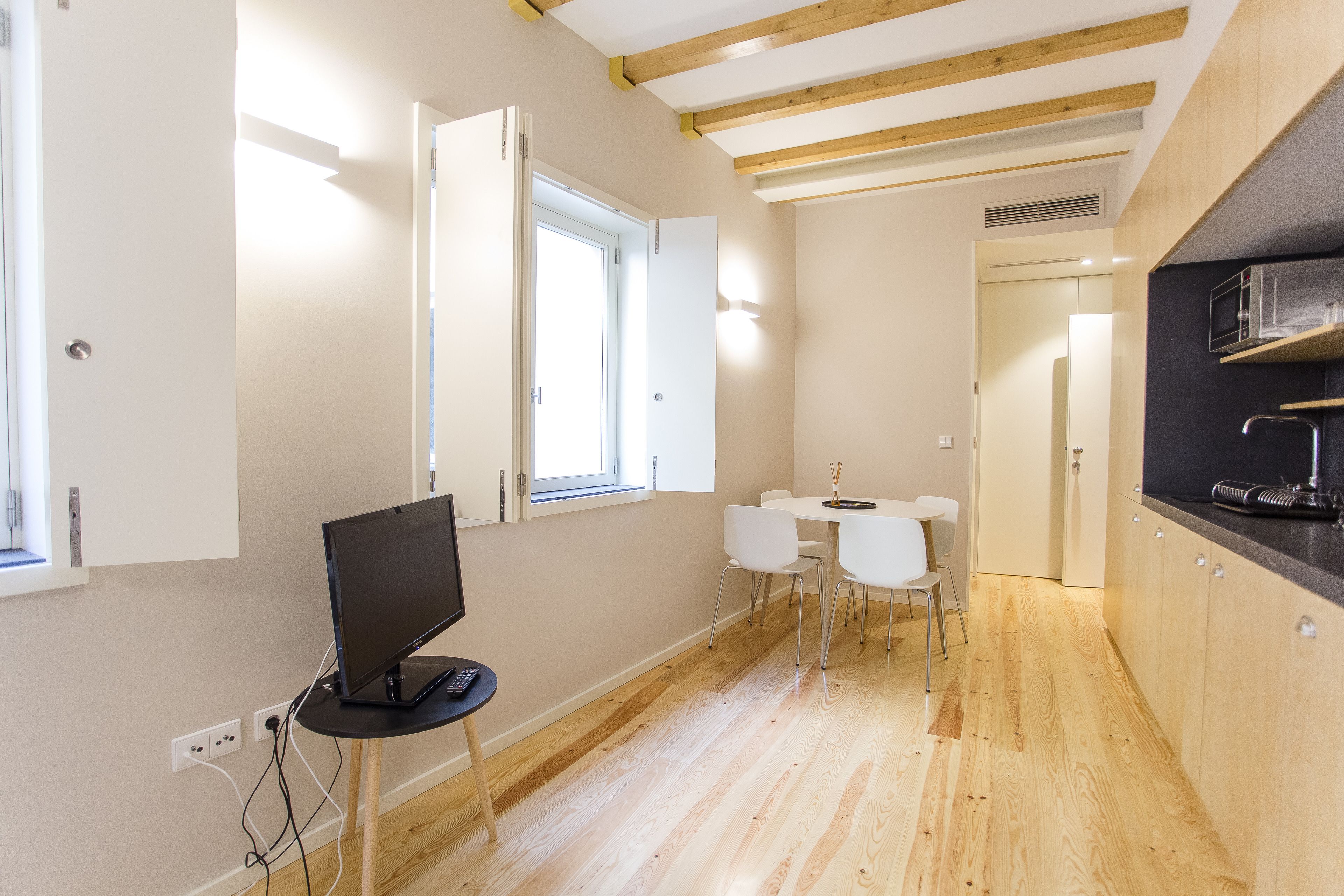 A modern kitchen with wooden beams, a dining area with white chairs, and a TV on a small table.