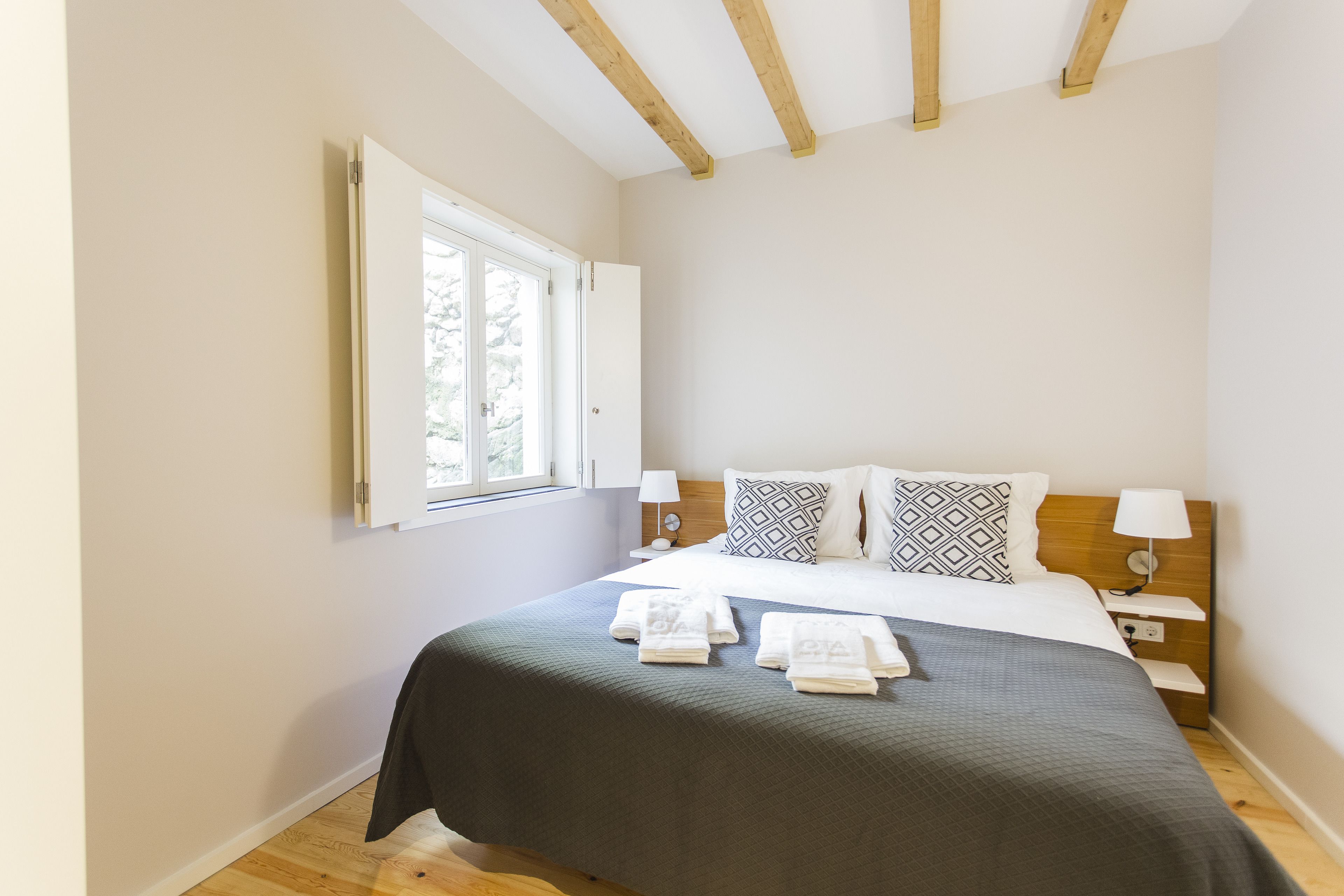 A bedroom with a bed, bedside tables, a window, and a wooden ceiling.