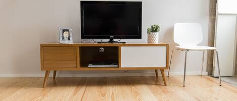 A modern living room with a wooden TV stand, a flat-screen TV, a small potted plant, a white chair, and a checkered rug.