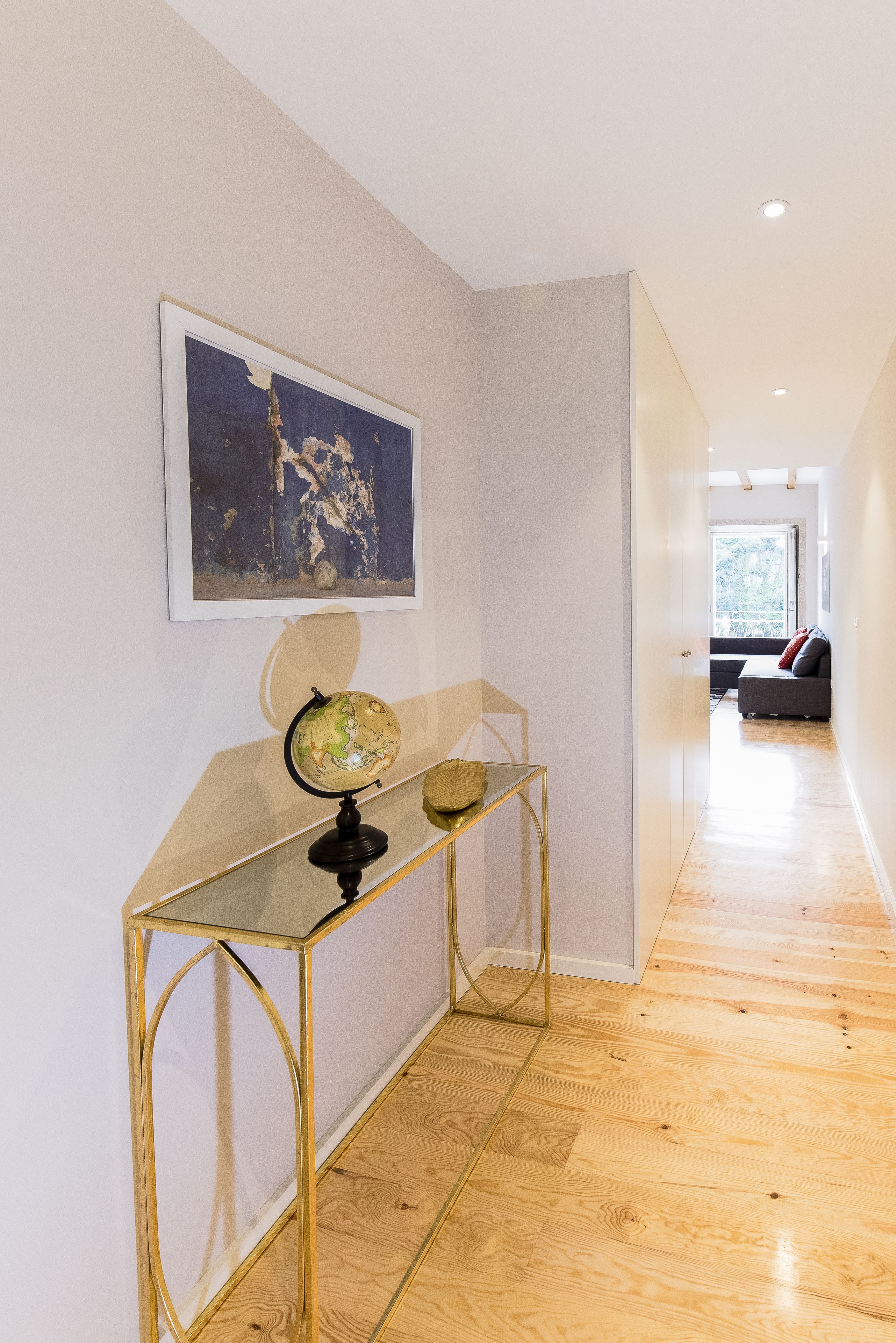 A hallway with a glass console table, a globe, and a framed abstract painting.