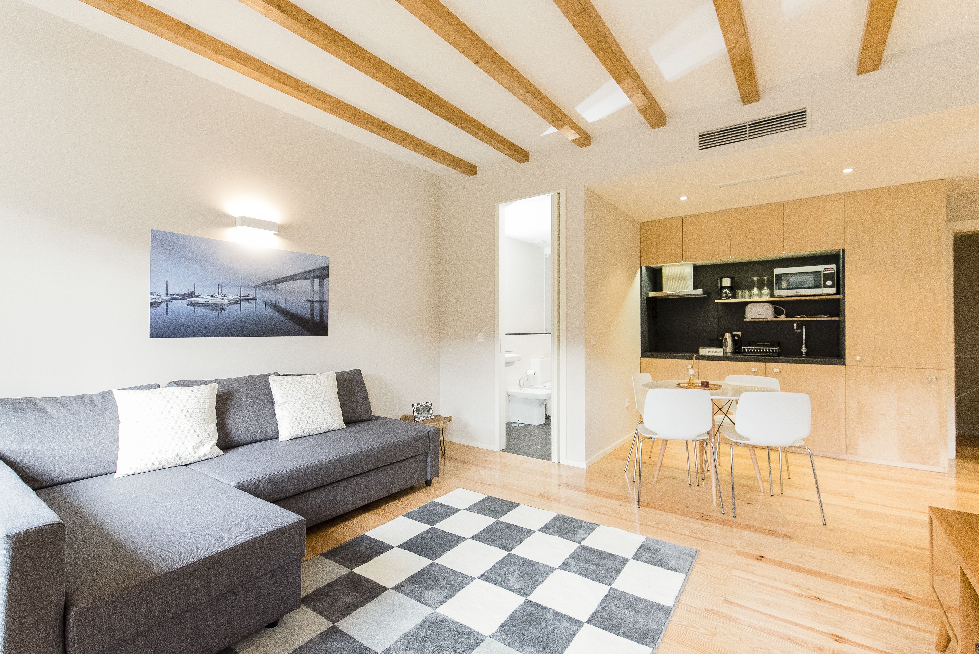 Un salon moderne avec un canapé d’angle gris, un tapis à carreaux noirs et blancs et un plafond en bois.