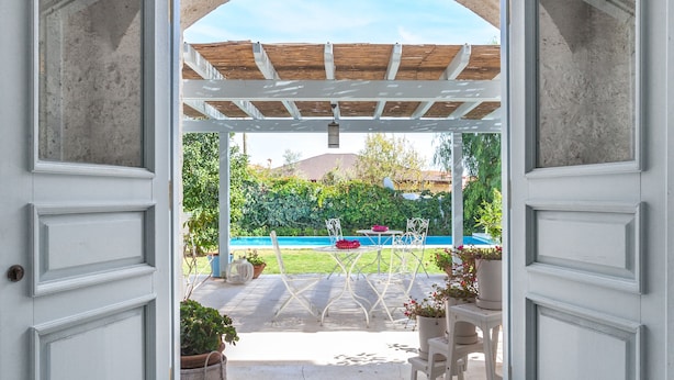 An open doorway leading to a covered patio area with a table and chairs, surrounded by potted plants and a view of a green landscape. - Alura Boutique Hotel (Cesme)