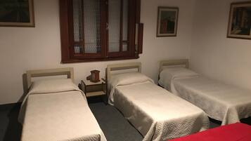 Una habitación con tres camas individuales, una mesita con lámpara y una ventana con persianas.