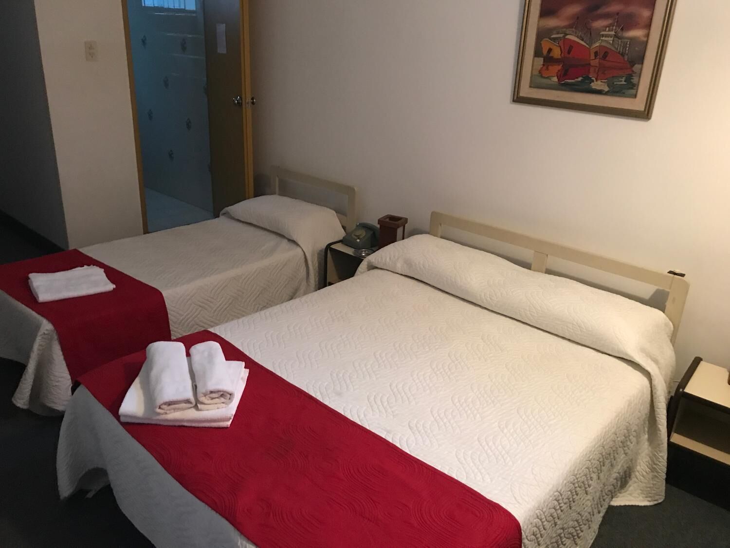 A hotel room with two beds, each with a red and white bedspread, and a painting on the wall.