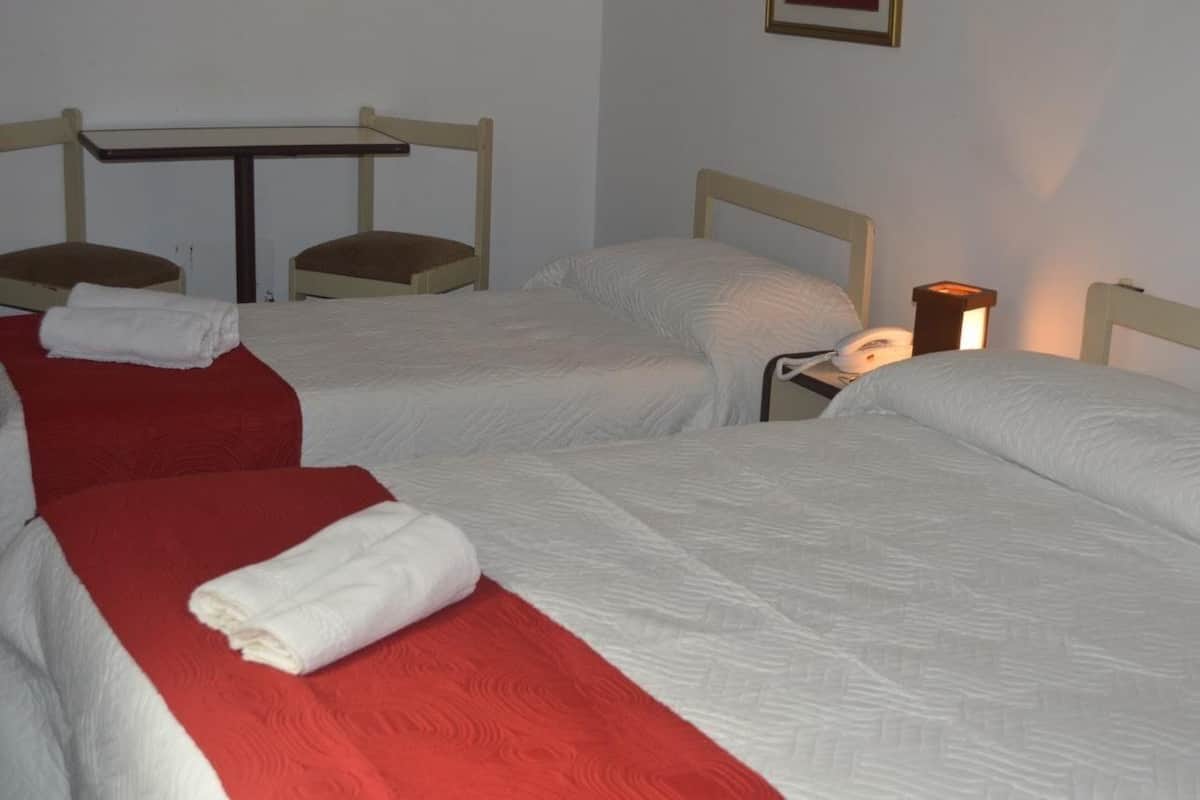 A hotel room with two single beds, each with a red and white bedspread, a small table, and a bedside lamp.