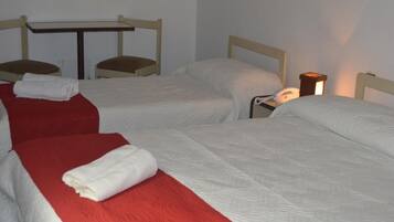 A hotel room with two single beds, each with a red and white bedspread, a small table, and a bedside lamp.