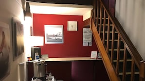 A hotel reception area with a red wall, a clock, a framed picture, and a sign with room rates. - Hotel Antares (Montevideo)