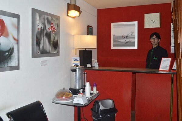 Un espace d’accueil d’hôtel avec un mur rouge, une horloge et une machine à café.