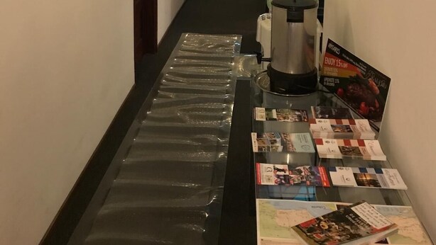 A hotel hallway with framed artwork on the walls, a water dispenser, and a magazine rack with brochures. - Hotel Antares (Montevideo)