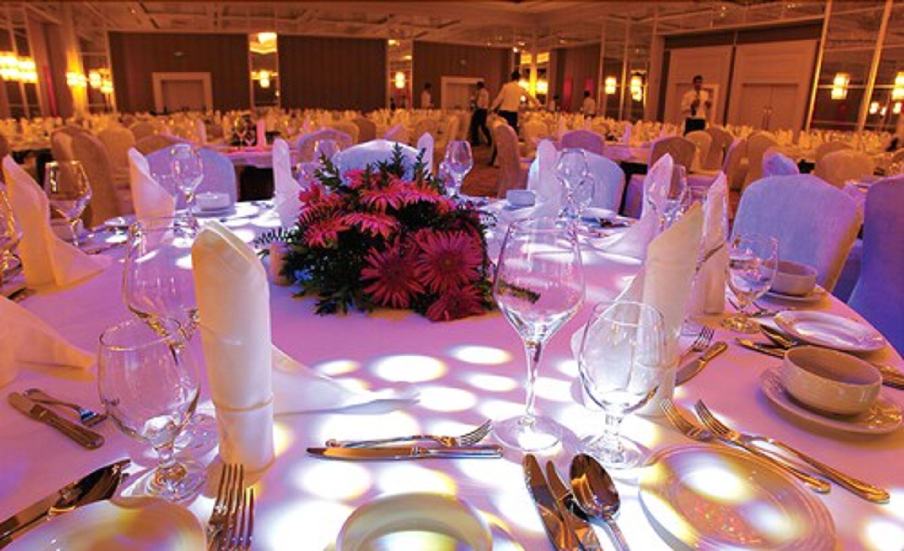 A banquet hall with round tables set for a formal event, featuring white tablecloths, floral centerpieces, and formal dining ware.