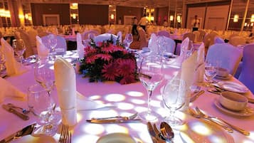 A banquet hall with round tables set for a formal event, featuring white tablecloths, floral centerpieces, and formal dining ware.