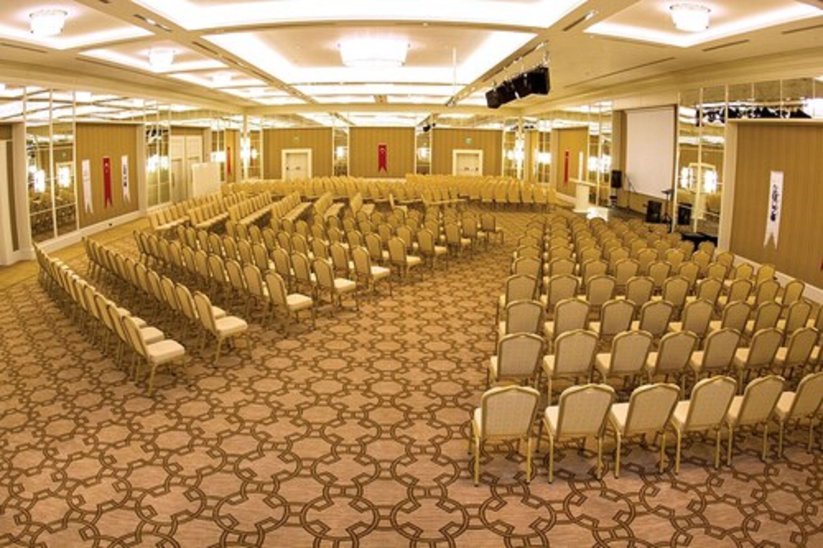 A large conference room with rows of chairs arranged in a semi-circle, carpeted floor, and a stage at the front.