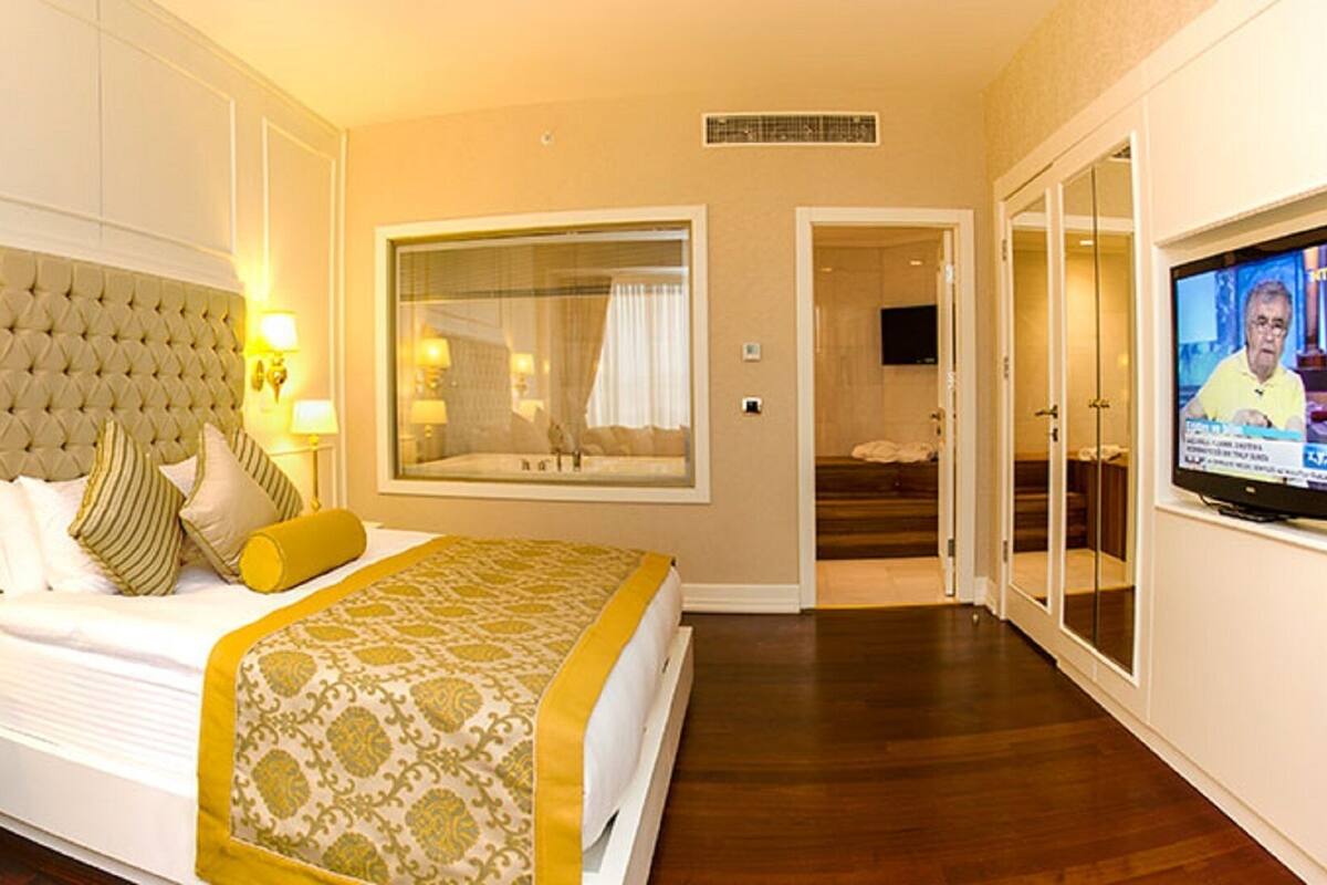 Una habitación de hotel con una cama grande, una zona de estar con una silla y una mesita, un televisor y un ventanal amplio.