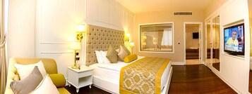 Una habitación de hotel con una cama grande, una zona de estar con una silla y una mesita, un televisor y un ventanal amplio.
