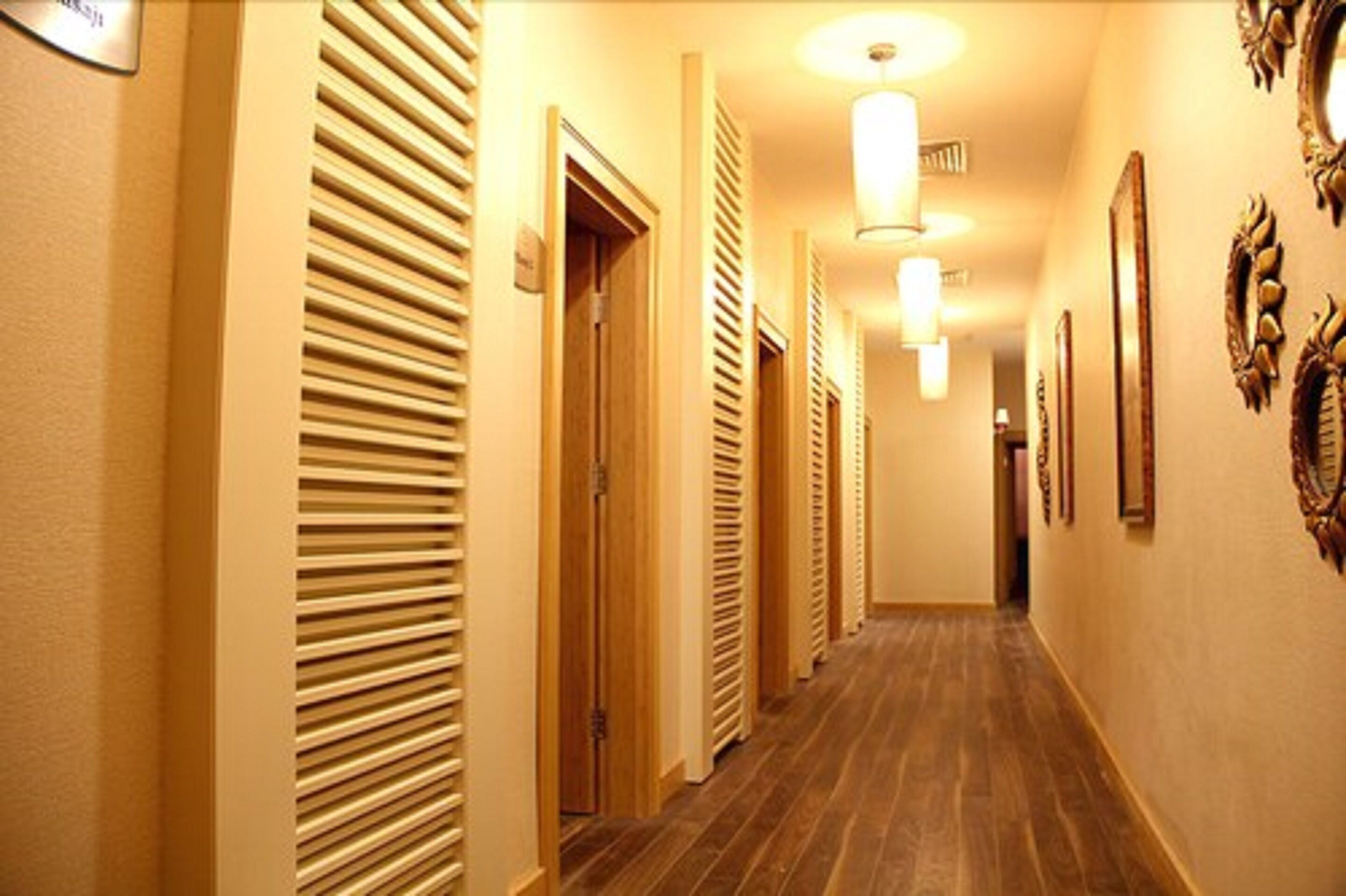 Un pasillo de hotel con pisos de madera, paredes color beige y puertas con listones horizontales.