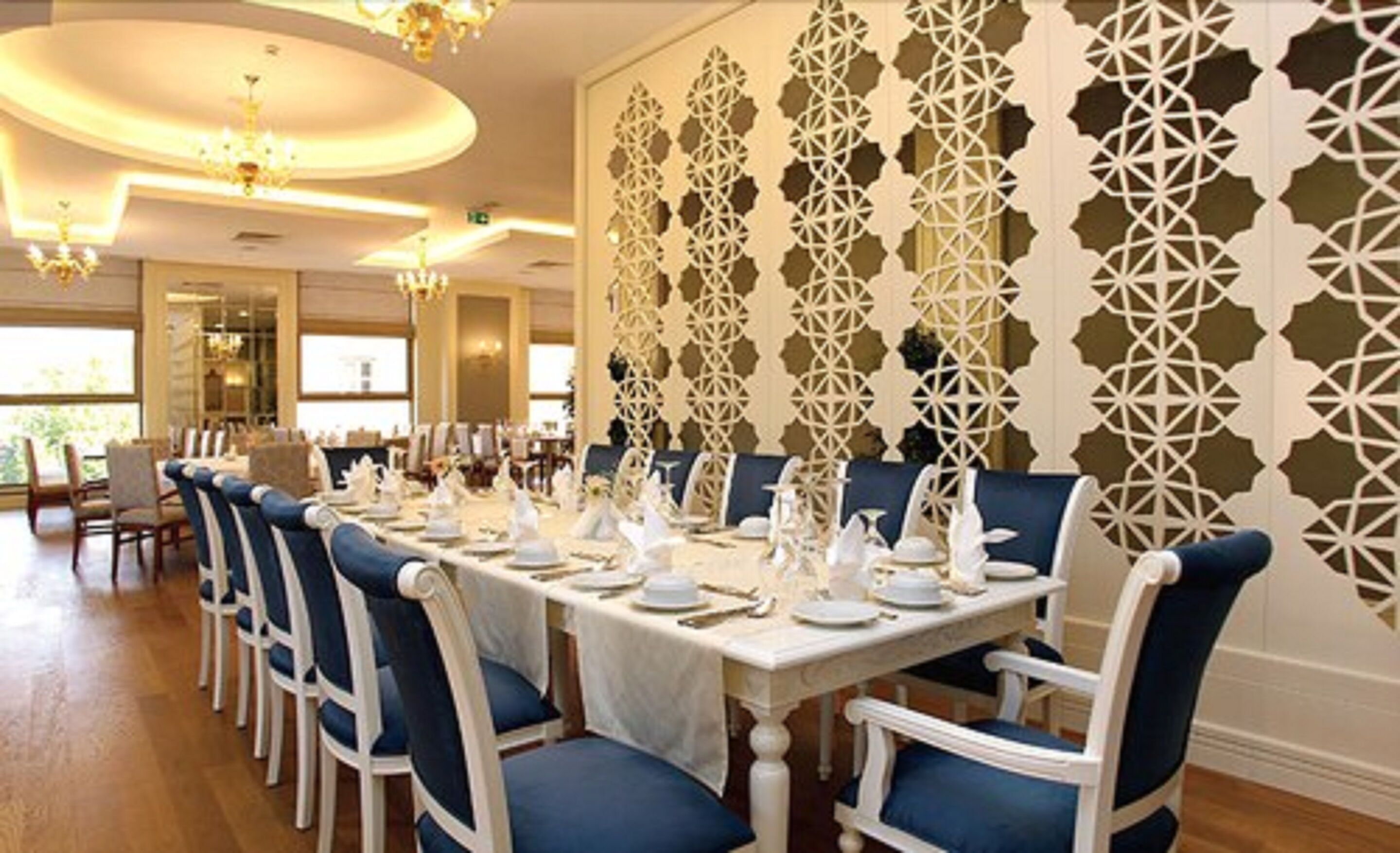 Een formele eetzaal met een lange tafel gedekt voor een maaltijd, omringd door blauwe fauteuils.