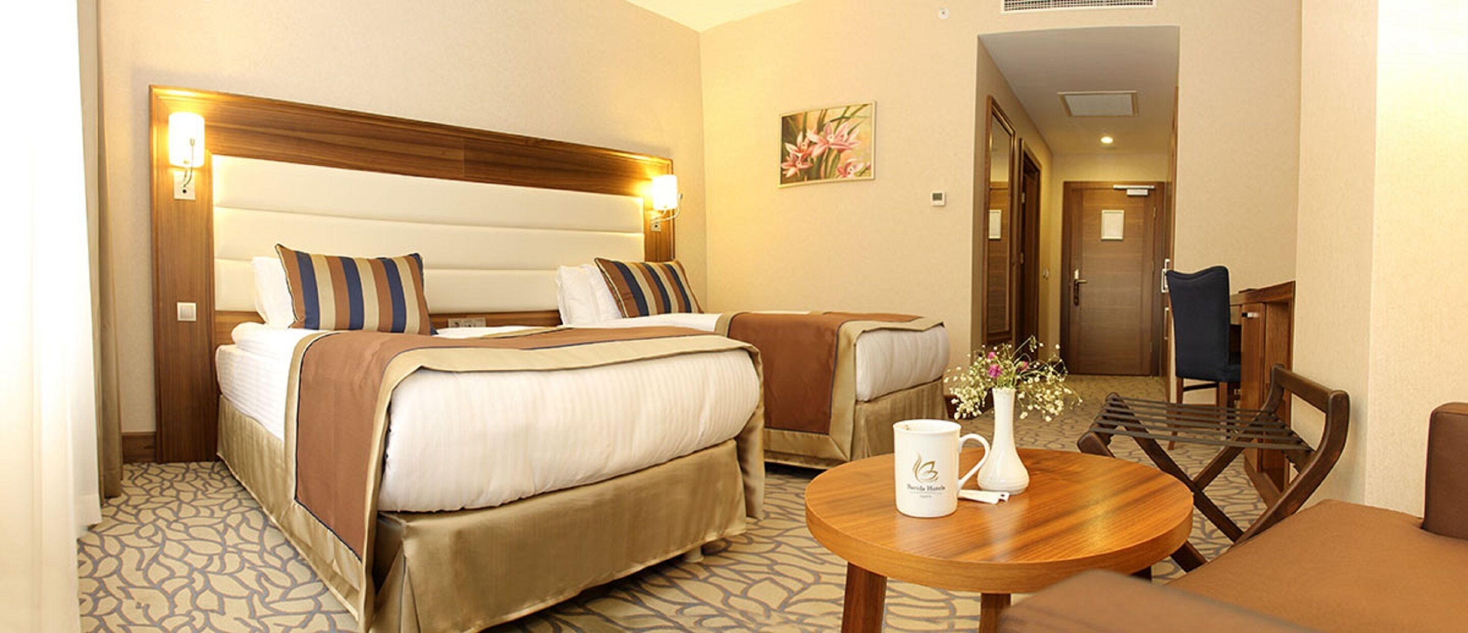 A hotel room with two beds, a small table with a vase, and a chair.