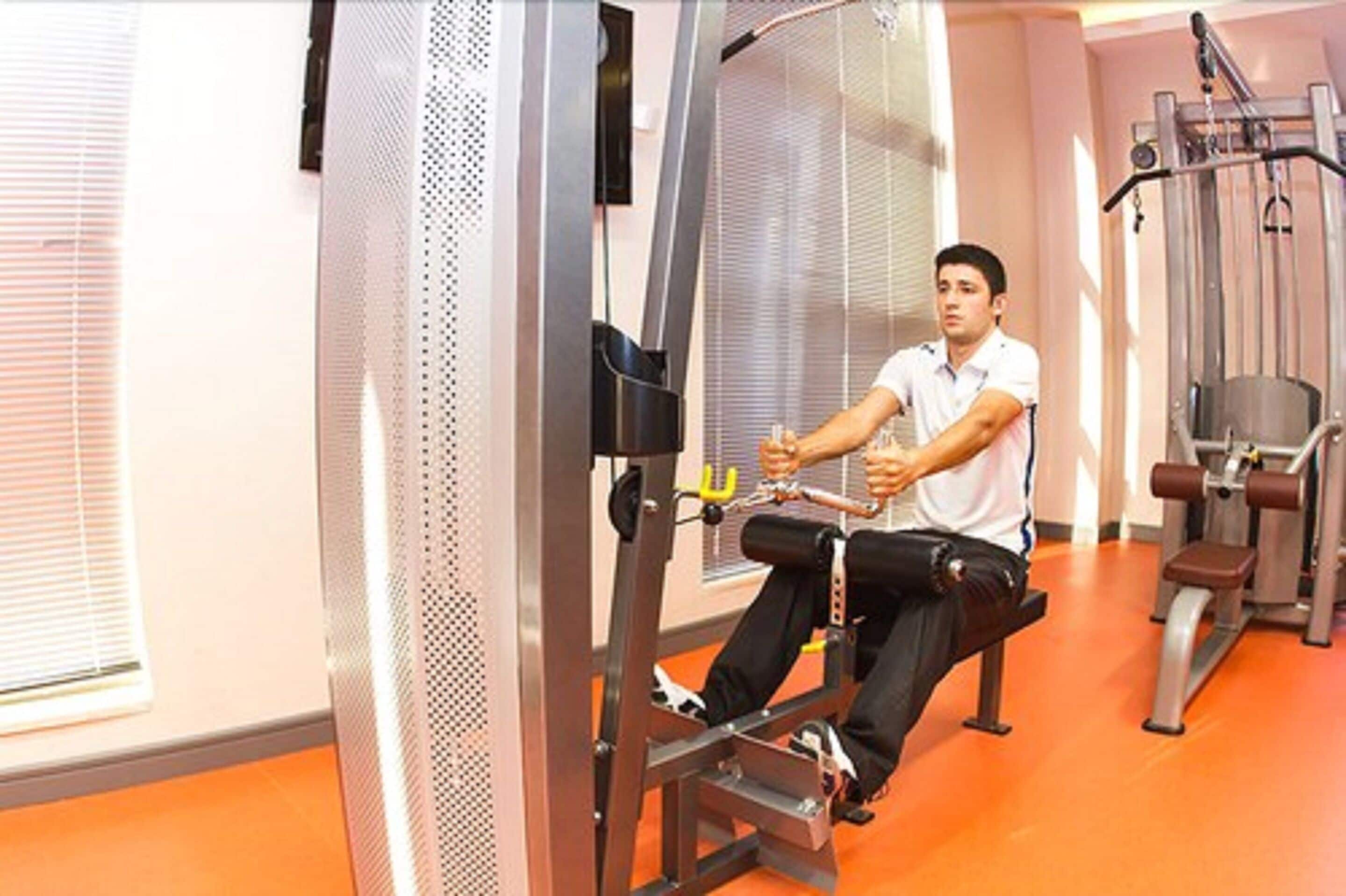A man using a cable machine in a gym with orange flooring and metal exercise equipment.