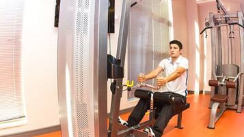 A man using a cable machine in a gym with orange flooring and metal exercise equipment.