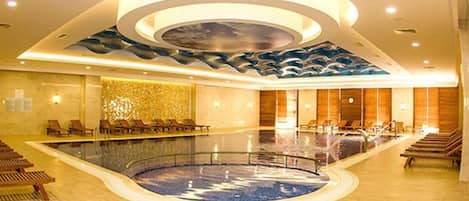Una amplia piscina interior de diseño circular, rodeada de sillones de descanso y un techo moderno con motivos de olas.