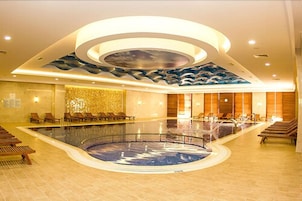Una amplia piscina interior de diseño circular, rodeada de sillones de descanso y un techo moderno con motivos de olas.