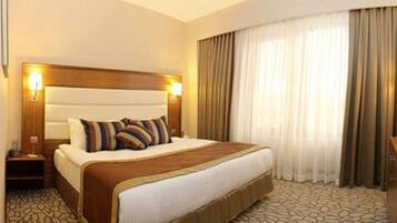 Una habitación de hotel con una cama grande, televisión, mesita de noche y ventana con cortinas.