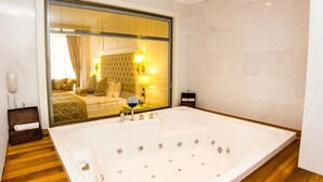 A spacious bathroom with a large bathtub, a mirror, and a bedside table.