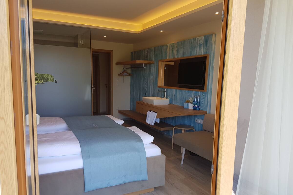A modern bedroom with a bed, a bench, a vanity with a mirror, and a shower area.