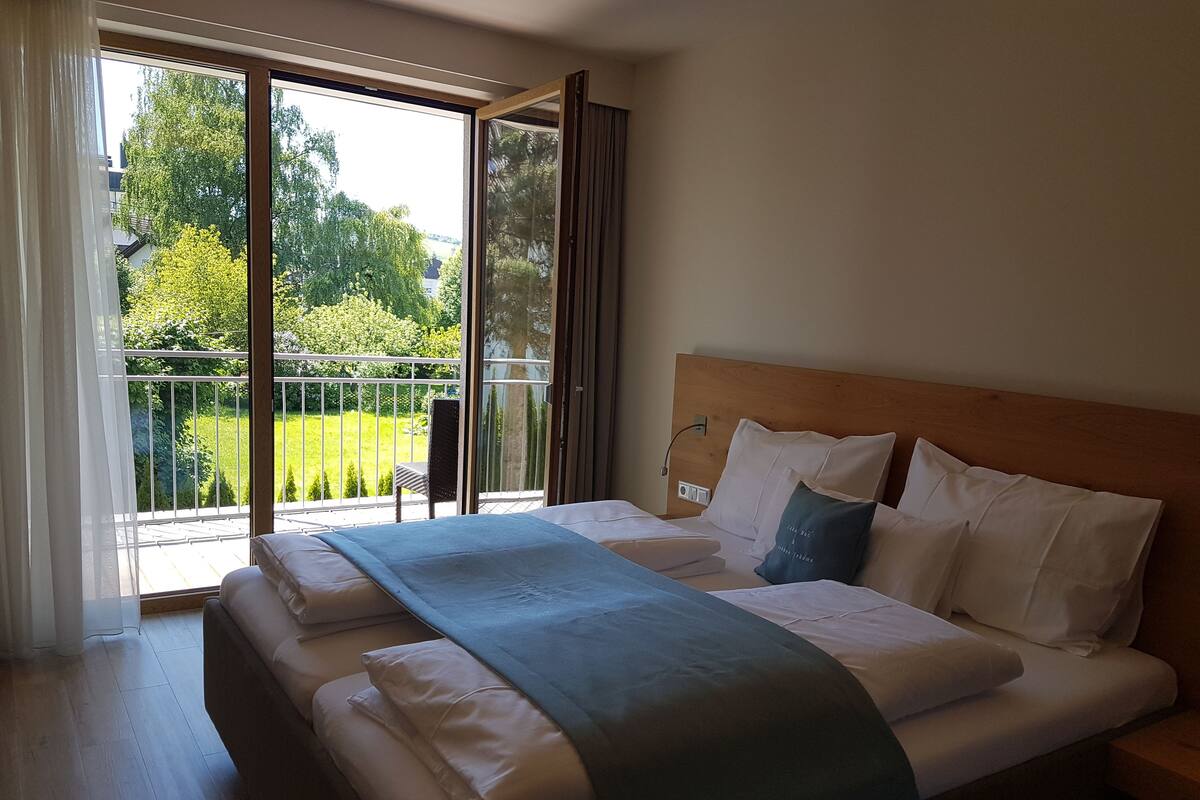 A bedroom with a large bed, a wooden headboard, and a view of a garden through a sliding glass door.