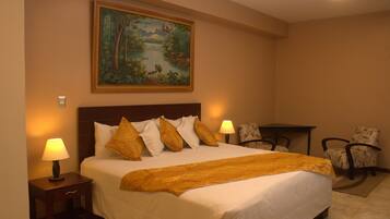 A hotel room with a large bed, two bedside lamps, a painting on the wall, a small table, and two chairs.