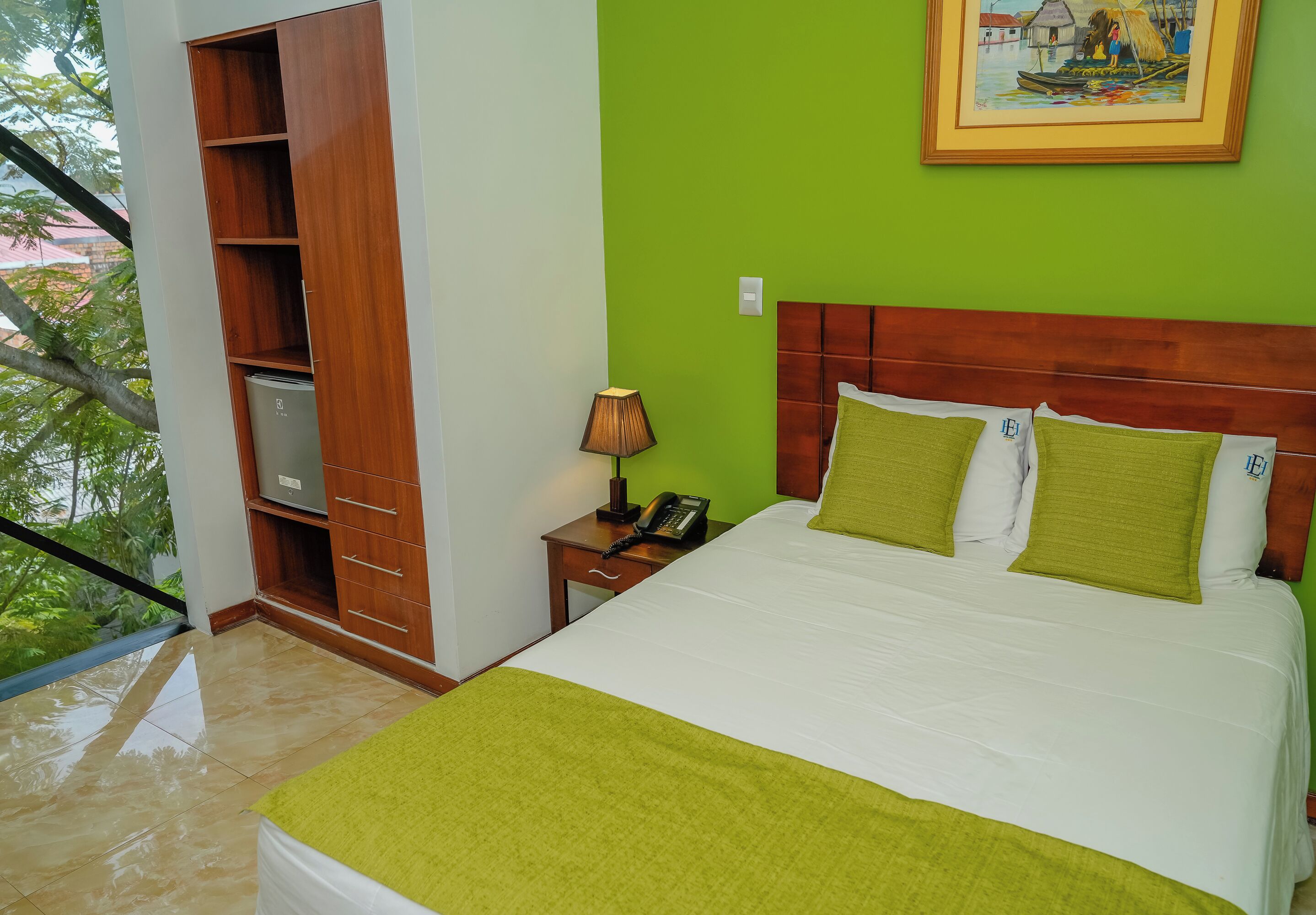 A hotel room with a bed, a nightstand, a lamp, a wooden wardrobe, and a green wall.