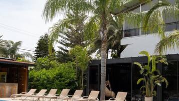 Una piscina con sillas de descanso, palmeras y un edificio moderno al fondo.