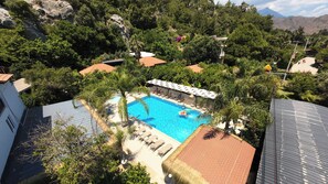 Una piscina rodeada de sillones de descanso y una zona cubierta, con montañas al fondo.